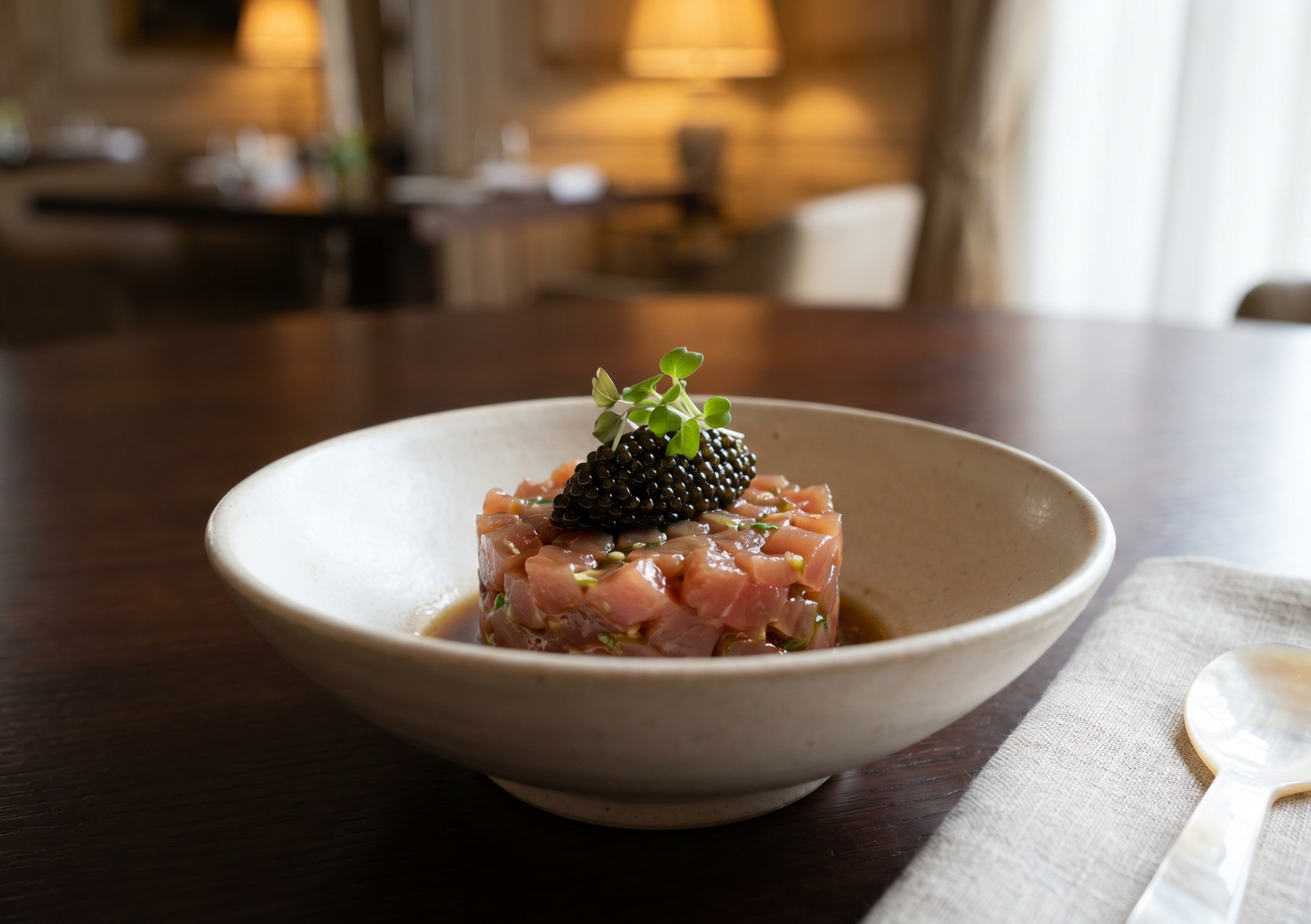 A beautiful, shallow ceramic bowl holding a perfectly round serving of fresh tuna tartare, generously crowned with caviar indonesia.