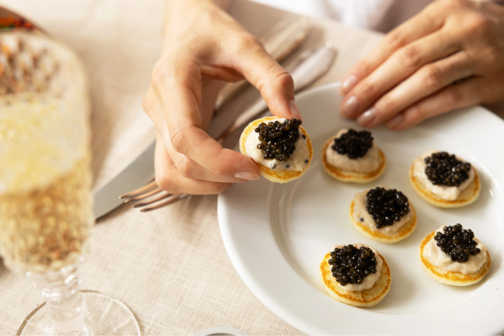 A hand holding blinis with Crème Fraîche and black caviar on top
