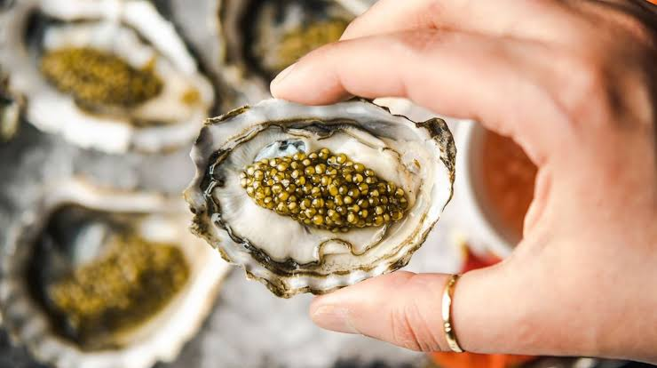 A hand holdiong an oyster with caviar on top