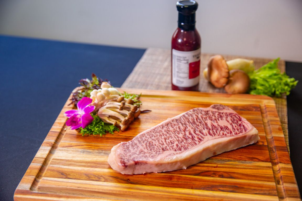A slab of Japanese Wagyu on a wooden board with a side bottle of sauce