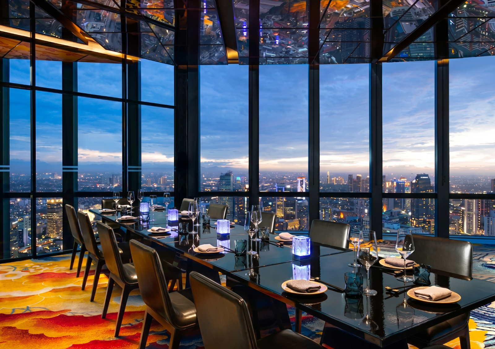 An elegant long dining table set for dinner in a high-rise restaurant with floor-to-ceiling windows, offering a spectacular twilight view of the city skyline, a perfect setting to enjoy Caviar indonesia.